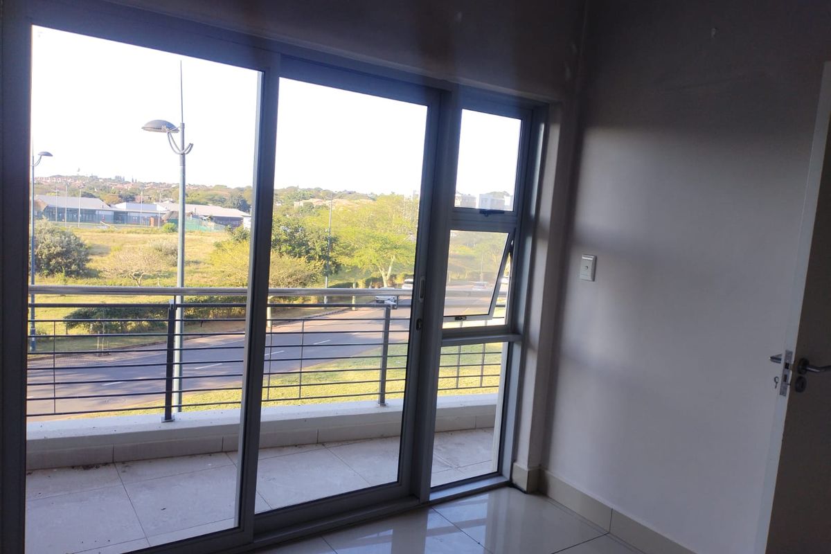 An empty living area featuring large sliding glass doors that open onto a balcony with views of the surrounding neighborhood.