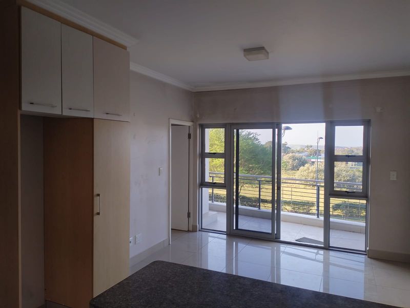 An empty open-plan living area featuring tiled floors, built-in cabinetry, and large sliding glass doors leading to a balcony with scenic views.