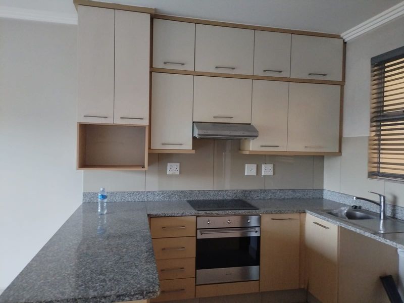 A functional kitchen featuring granite countertops, built-in oven, electric hob, extractor fan, and ample fitted cabinetry with a neutral finish.