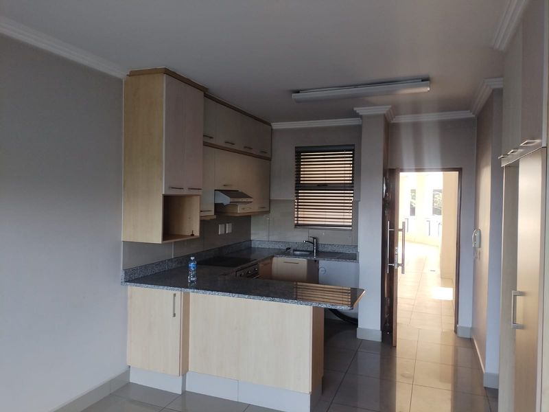 A clean, functional kitchen featuring light wood cabinetry, granite countertops, and tiled flooring, offering a practical layout for modern apartment living.