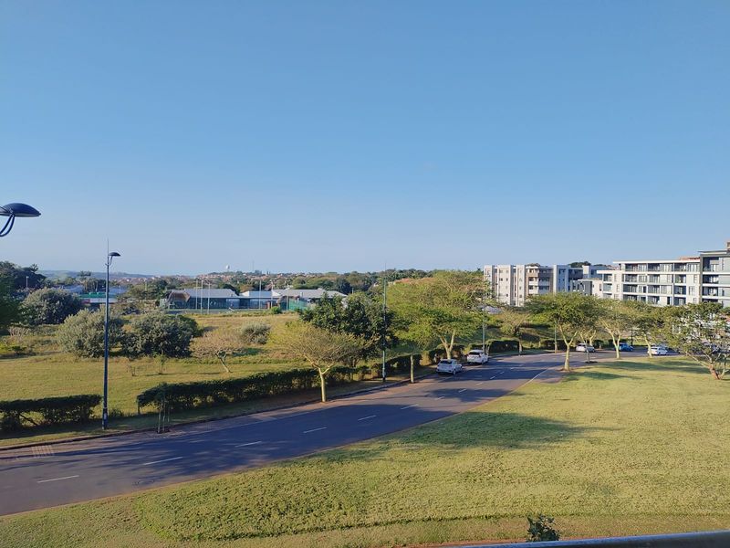 An elevated view overlooking the surrounding neighbourhood, featuring landscaped green spaces, a paved road, and nearby residential apartment buildings.