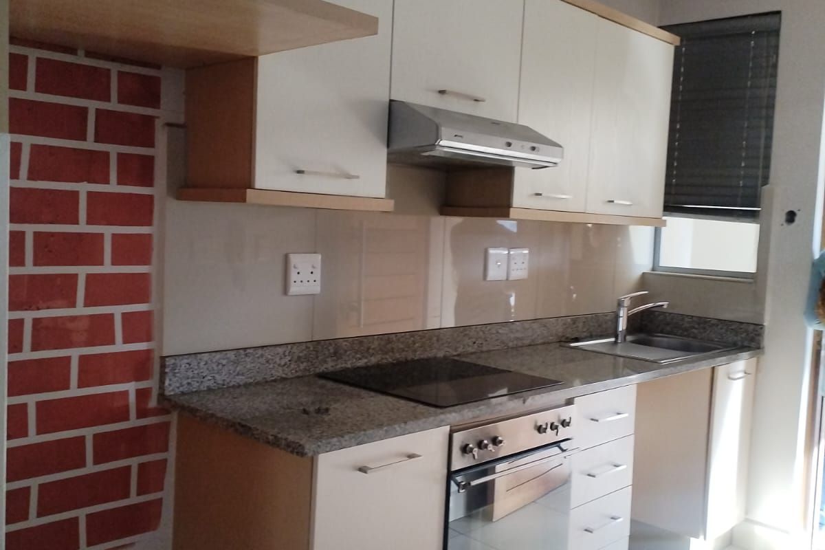 Modern kitchen featuring granite countertops, built-in oven, electric hob, extractor fan, and ample cabinetry, with a distinctive brick-effect feature wall.