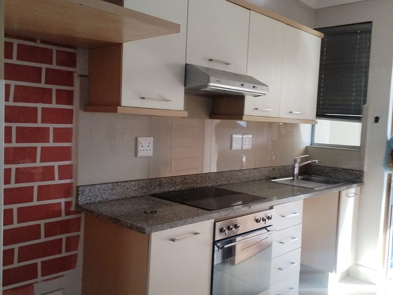 Modern kitchen featuring granite countertops, built-in oven, electric hob, extractor fan, and ample cabinetry, with a distinctive brick-effect feature wall.