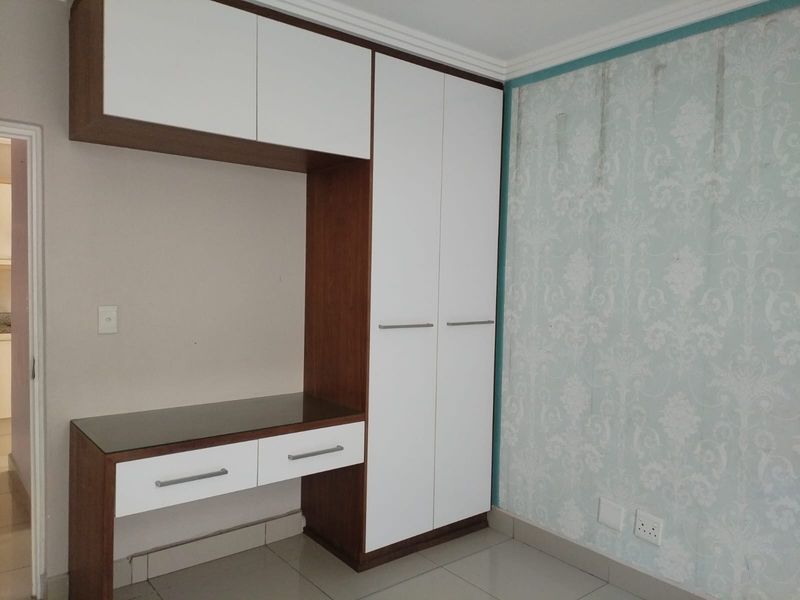 A bedroom featuring a built-in wardrobe and integrated desk unit, with tiled flooring and decorative wallpaper requiring attention.