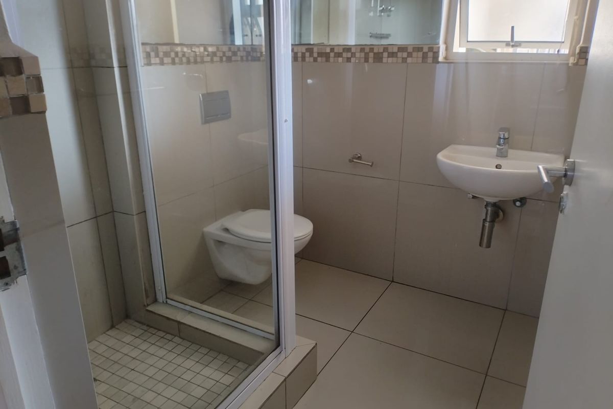 A clean, modern bathroom featuring a wall-hung toilet, glass shower enclosure, and wall-mounted basin with neutral tiled finishes.