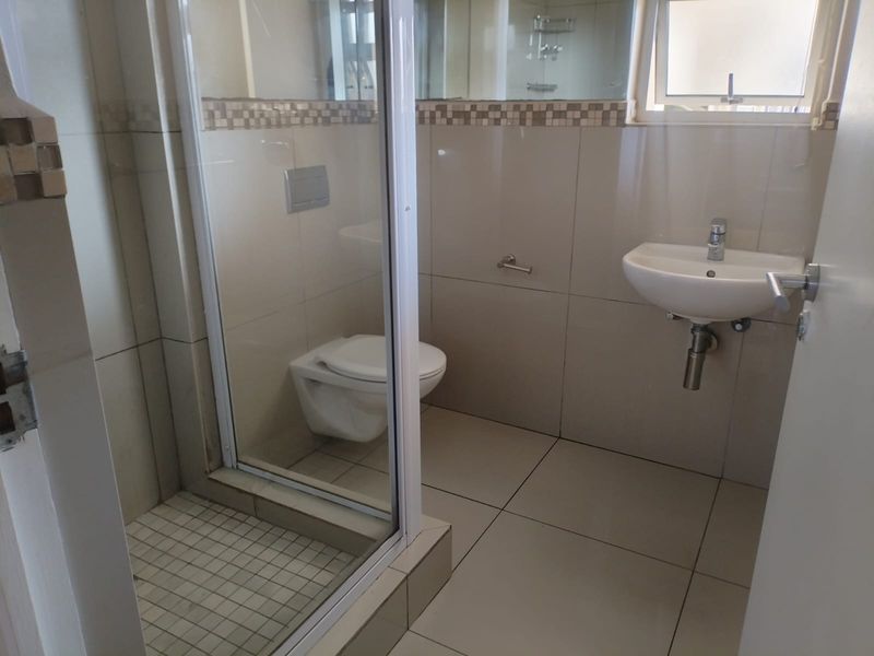 A clean, modern bathroom featuring a wall-hung toilet, glass shower enclosure, and wall-mounted basin with neutral tiled finishes.