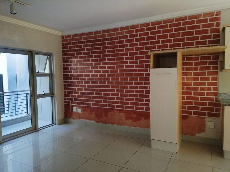 Open plan living area featuring tiled floors, a sliding door to the balcony, and a partially finished brick-effect feature wall with built-in cabinetry.