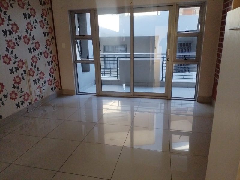 An empty living room featuring large format floor tiles, a decorative feature wall, and sliding glass doors providing access to an outdoor balcony area.