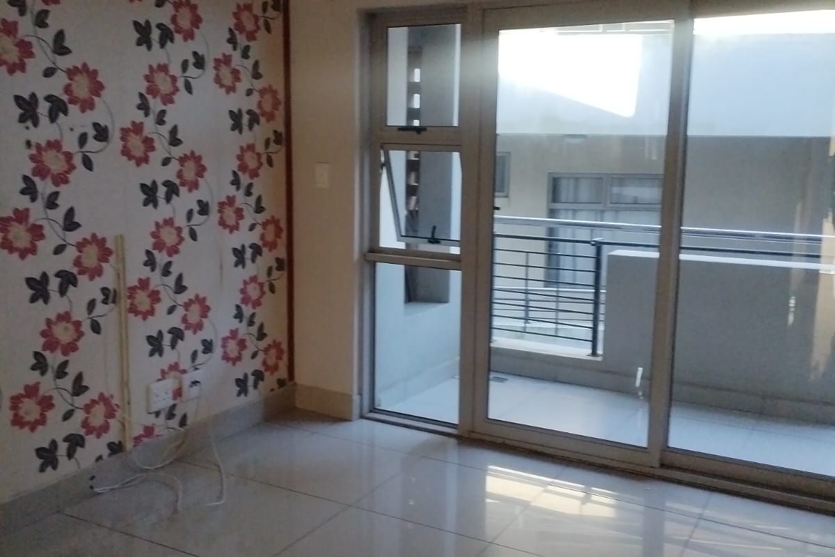An empty living room featuring large format floor tiles, a decorative floral feature wall, and sliding glass doors leading to an outdoor balcony.