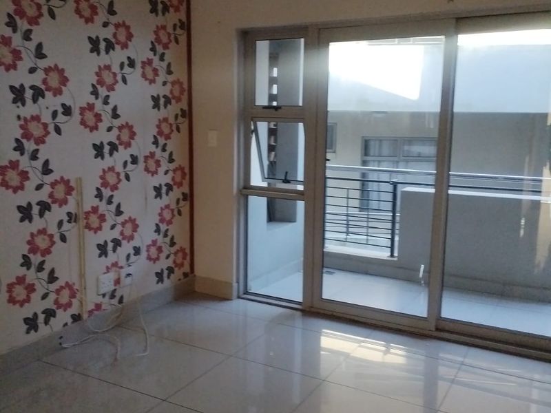 An empty living room featuring large format floor tiles, a decorative floral feature wall, and sliding glass doors leading to an outdoor balcony.