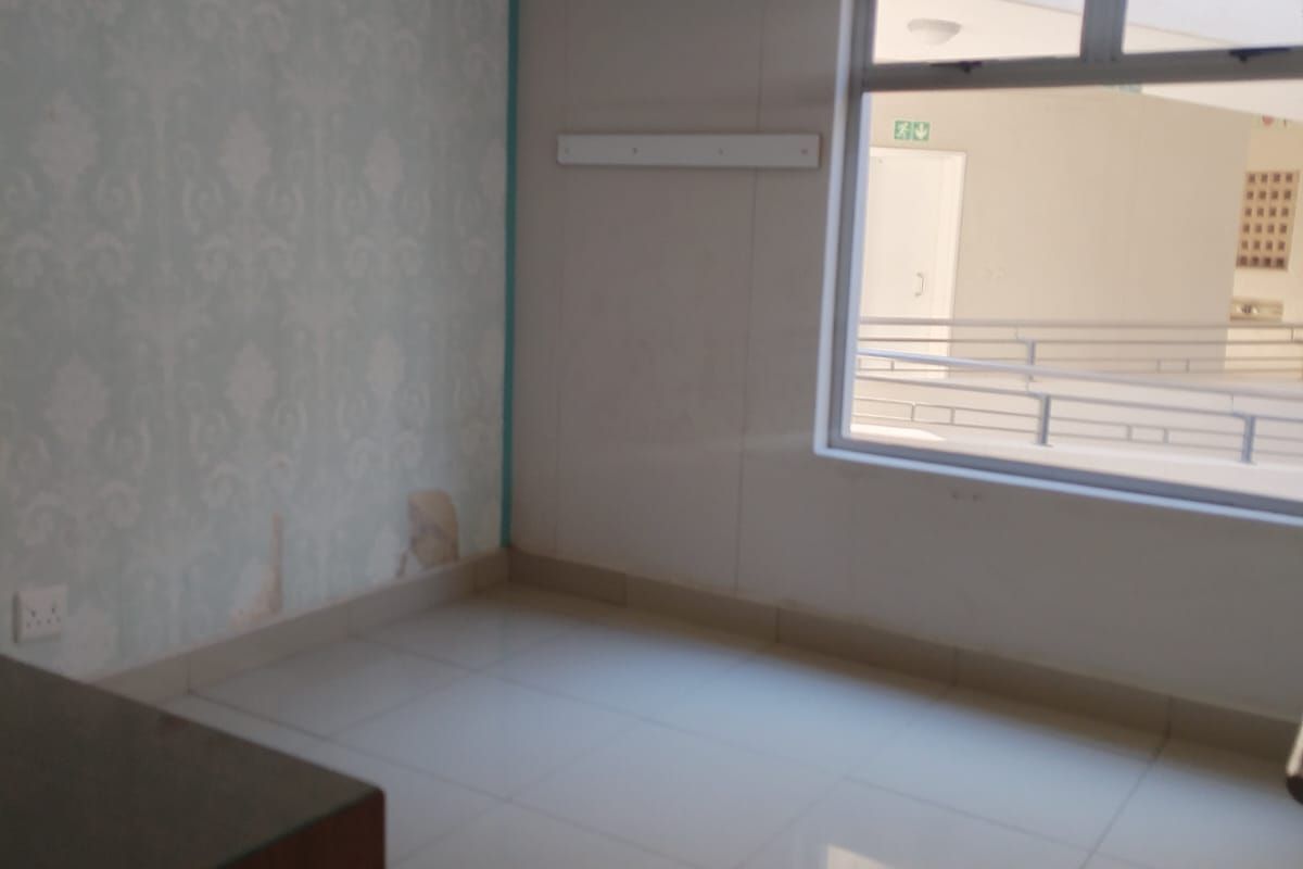 An empty bedroom featuring tiled flooring, a large window, and a feature wall with damaged wallpaper requiring repair.
