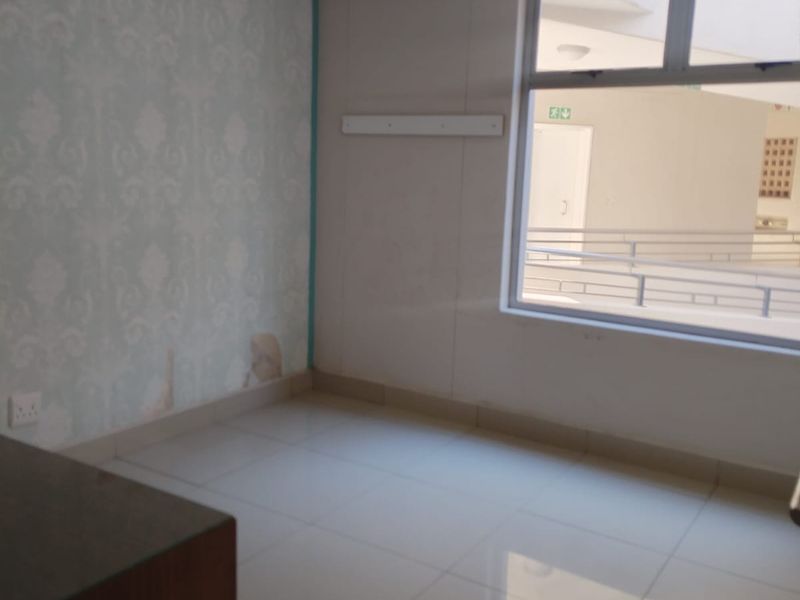 An empty bedroom featuring tiled flooring, a large window, and a feature wall with damaged wallpaper requiring repair.