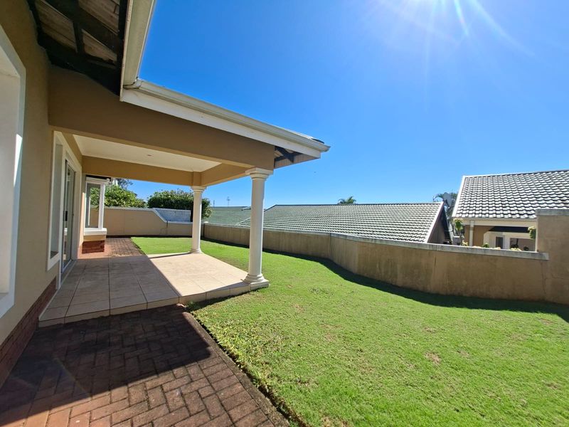 A covered patio area featuring tiled flooring and support columns, overlooking a private garden with a boundary wall.