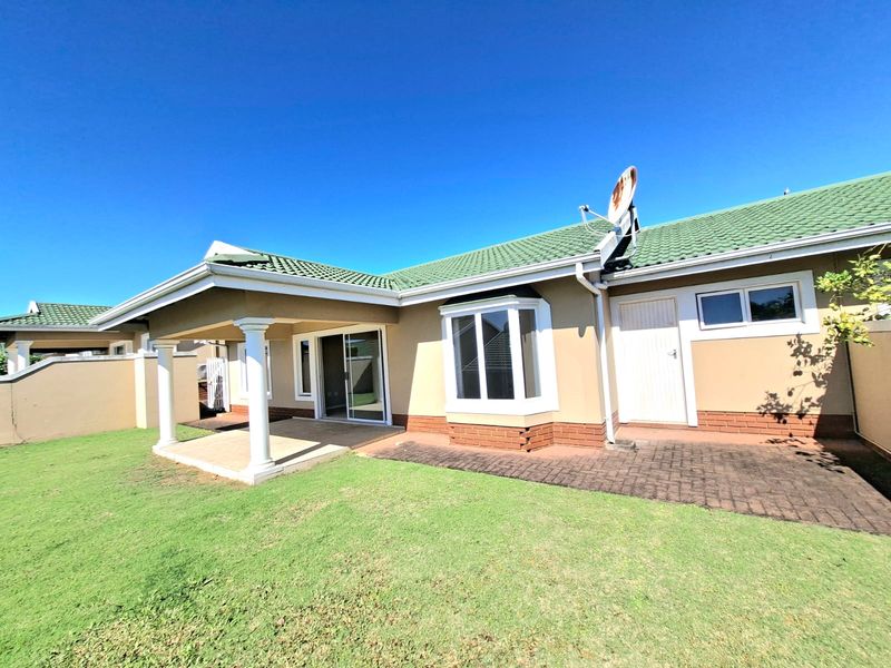 Rear view of the house featuring a covered patio, bay window, and paved area leading to a well-maintained lawn.