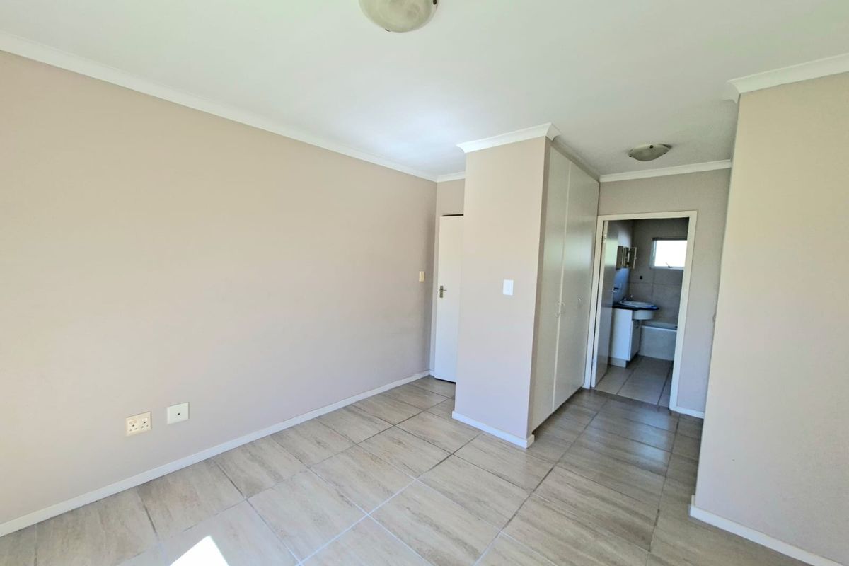 An empty bedroom featuring neutral wall paint, tiled flooring, and built-in cupboards, with an adjoining bathroom visible through the doorway.