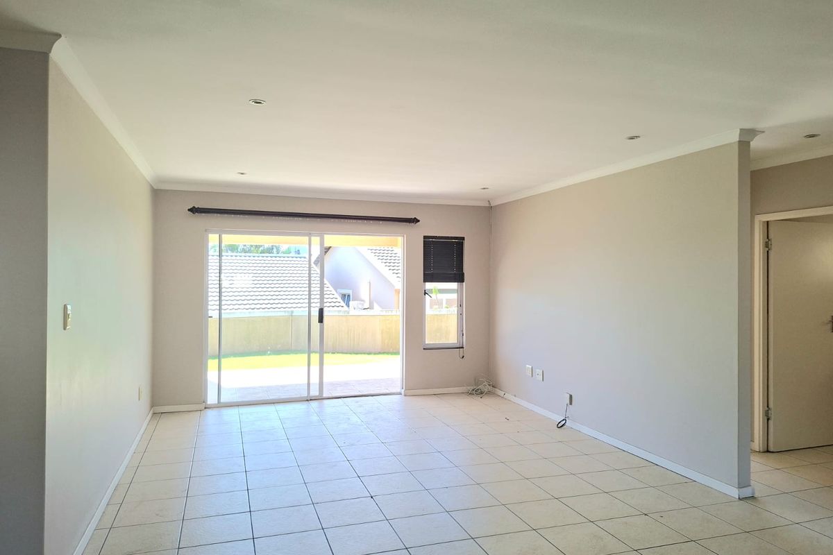 Spacious, light-filled living area featuring neutral tiled flooring, recessed lighting, and large sliding glass doors providing direct access to the outdoor patio.