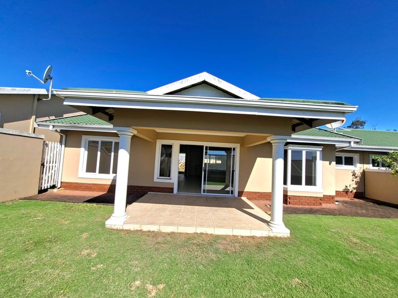 Rear view of the house featuring a covered tiled patio with decorative columns, sliding glass doors, and a well-maintained lawn.