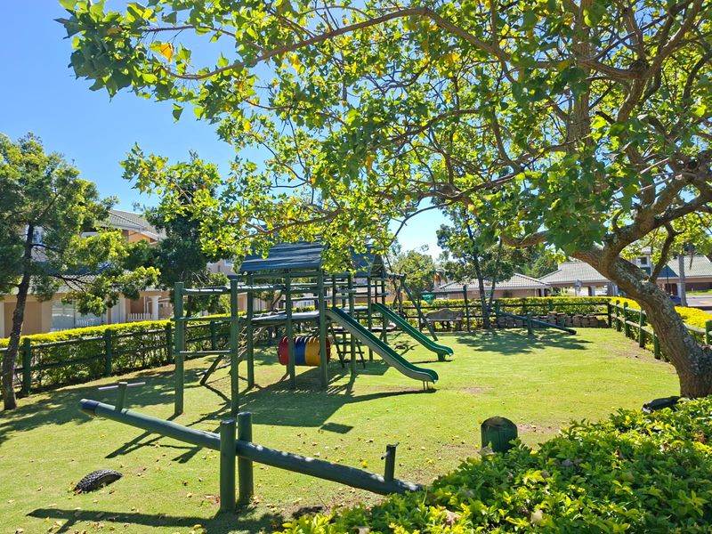 A well-maintained communal garden area featuring a children's playground, mature trees, and established lawn, enclosed by timber fencing.