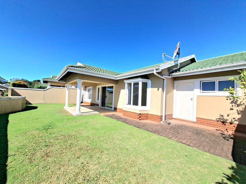 Rear view of the property featuring a covered patio, paved walkway, bay window, and a well-maintained lawn area.