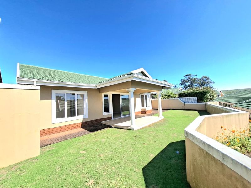 Rear view of the property featuring a covered patio, well-maintained lawn, and boundary wall, providing a private outdoor space.