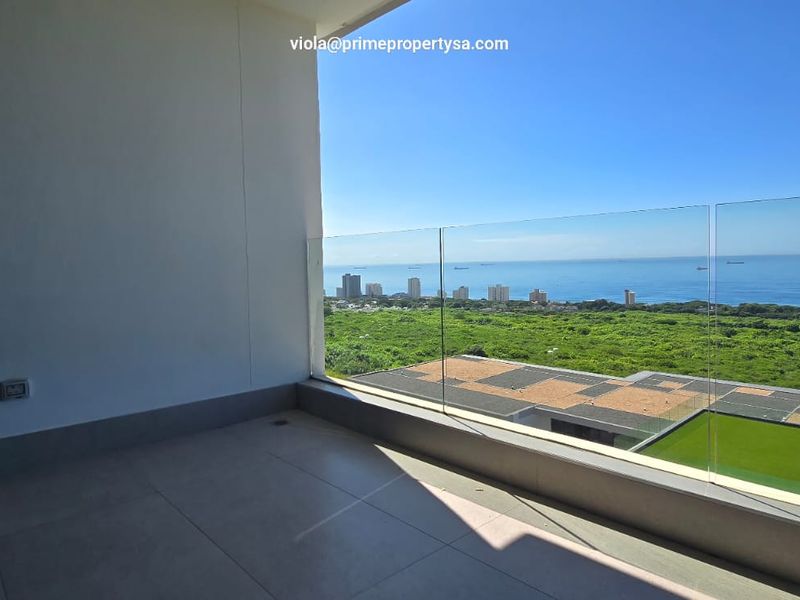A spacious balcony featuring a modern frameless glass balustrade and tiled flooring, offering expansive coastal and landscape views.
