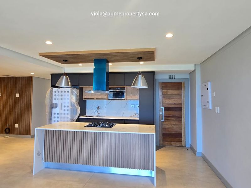Modern open-plan kitchen featuring a central island with gas hob, sleek cabinetry, stone countertops, and stylish timber slat wall accents.