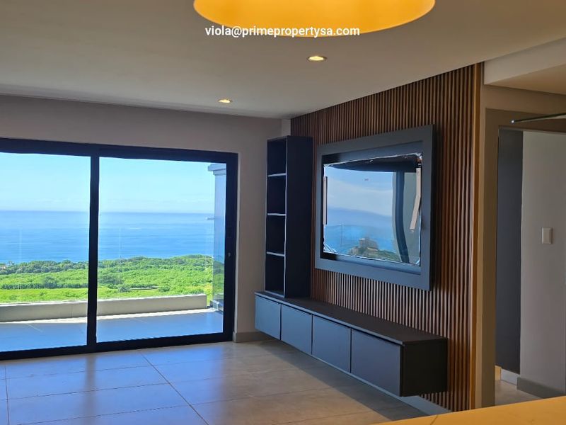 Modern open-plan living area featuring sleek slatted wood wall paneling, built-in cabinetry, and large sliding doors opening to a scenic ocean view.