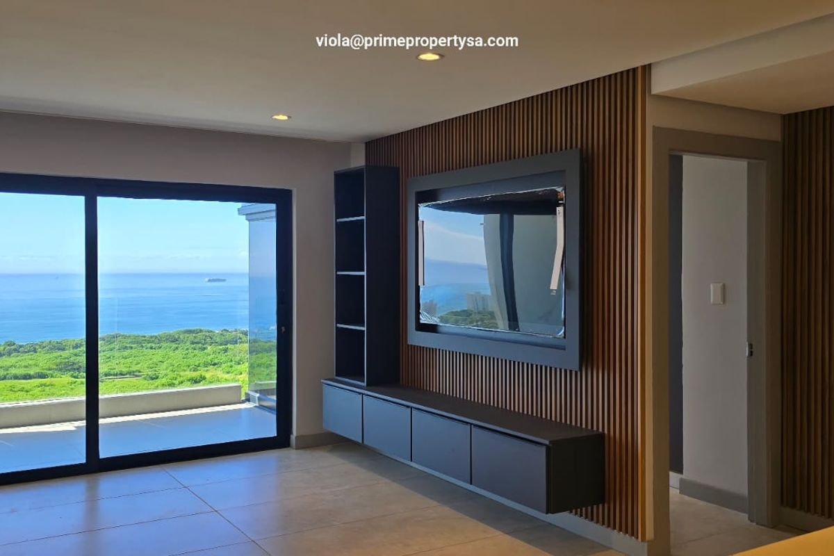 Modern living area featuring contemporary slat wood wall paneling, a built-in media console, and large sliding doors opening to a scenic ocean view.