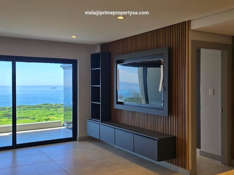 Modern living area featuring contemporary slat wood wall paneling, a built-in media console, and large sliding doors opening to a scenic ocean view.