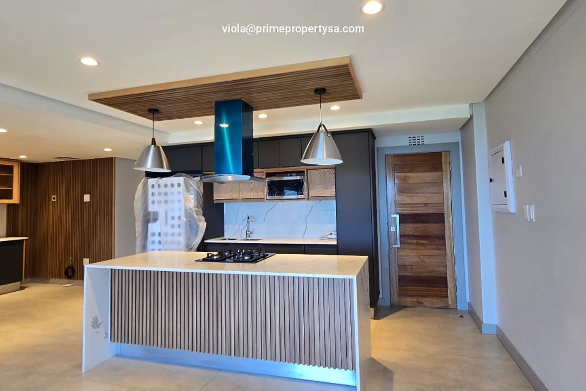 Modern open-plan kitchen featuring a central island with gas hob, sleek dark cabinetry, stone countertops, and stylish timber slat detailing.