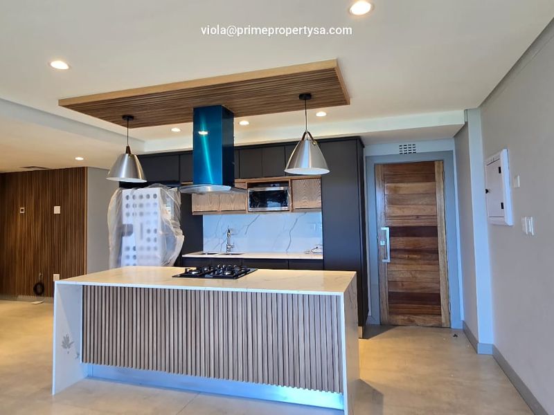 Modern open-plan kitchen featuring a central island with gas hob, sleek dark cabinetry, stone countertops, and stylish timber slat detailing.