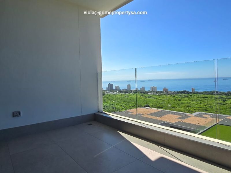 A spacious, modern balcony featuring a frameless glass balustrade and expansive coastal views, providing a seamless transition to the outdoors.
