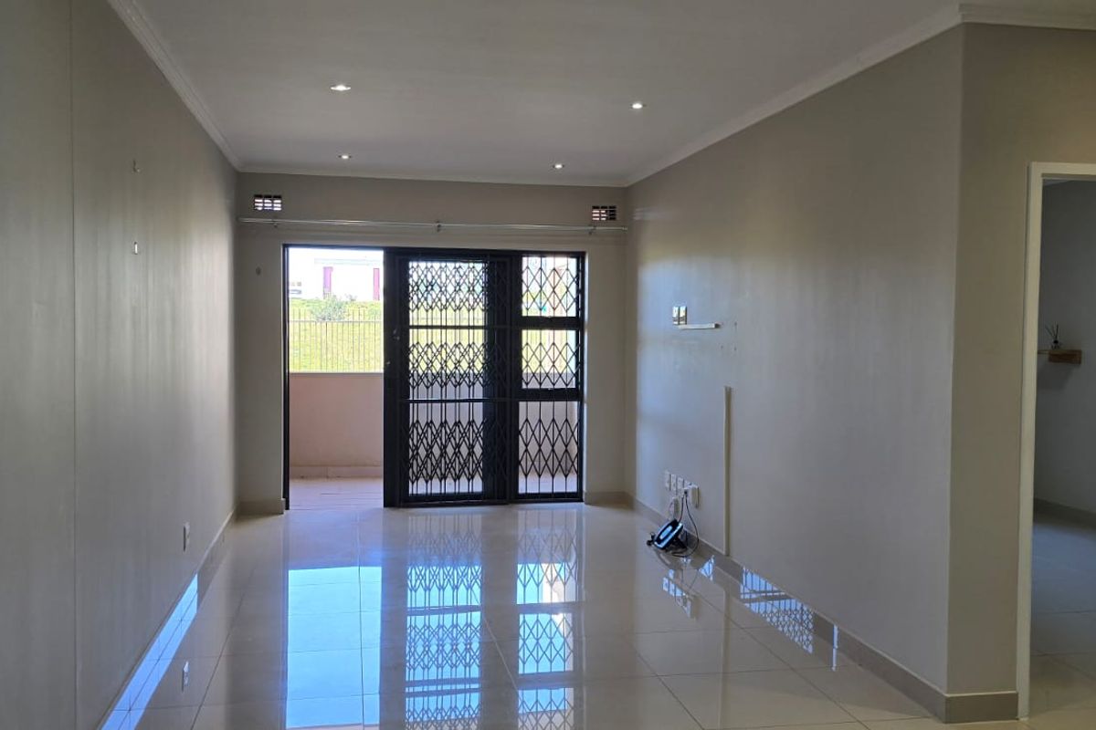 A bright, empty living area featuring polished tiled floors, recessed lighting, and a sliding glass door leading to an outdoor space with security gate.