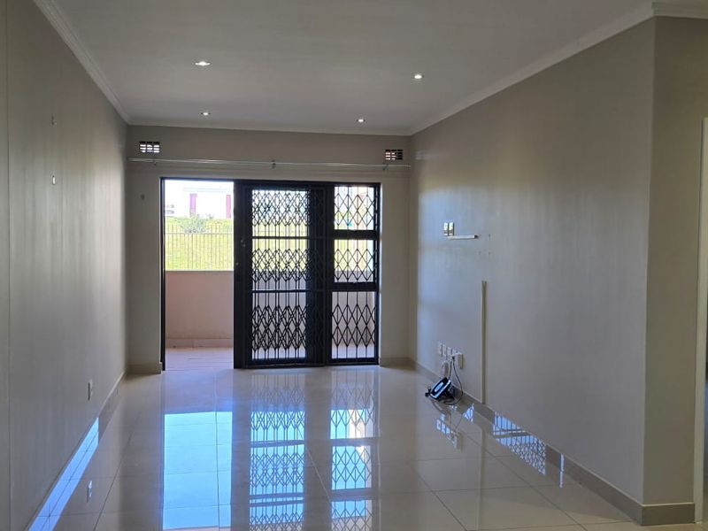 A bright, empty living area featuring polished tiled floors, recessed lighting, and a sliding glass door leading to an outdoor space with security gate.