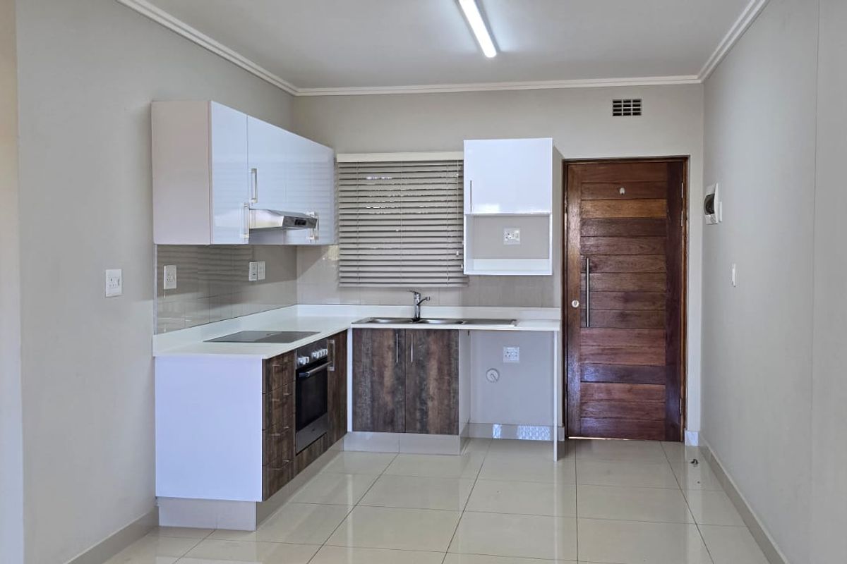 A clean, modern kitchen featuring built-in cabinetry, an electric hob, oven, extractor fan, and tiled flooring, presented in an empty, well-maintained space.