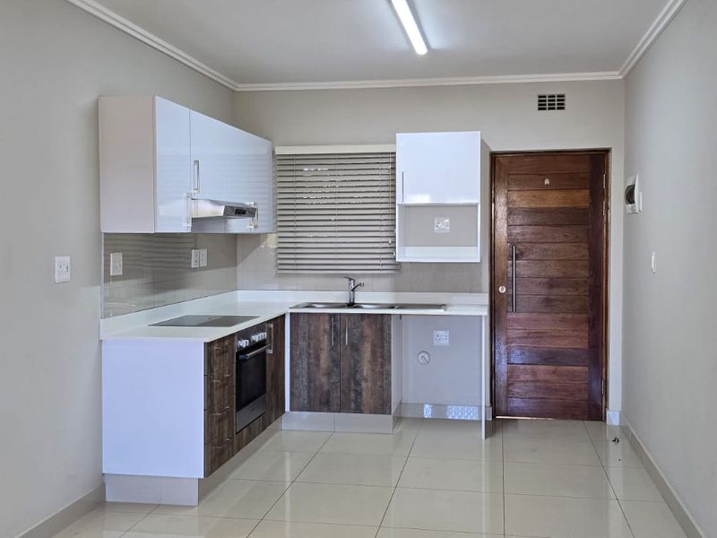 A clean, modern kitchen featuring built-in cabinetry, an electric hob, oven, extractor fan, and tiled flooring, presented in an empty, well-maintained space.
