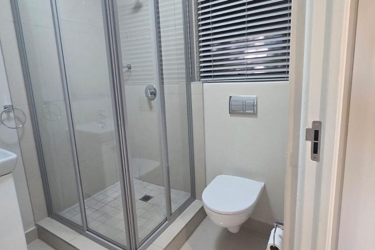 A clean, modern bathroom featuring a glass shower enclosure, wall-mounted toilet, and a vanity basin with contemporary fixtures.