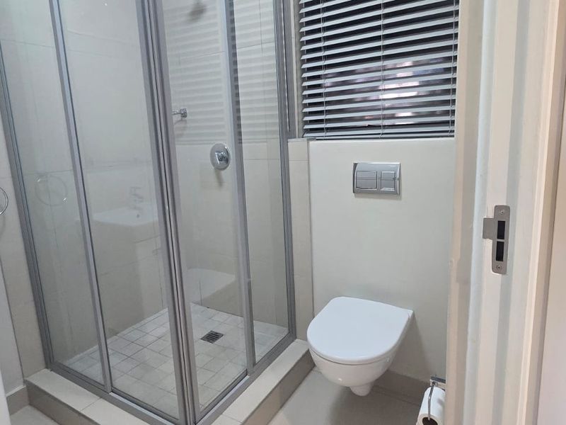 A clean, modern bathroom featuring a glass shower enclosure, wall-mounted toilet, and a vanity basin with contemporary fixtures.