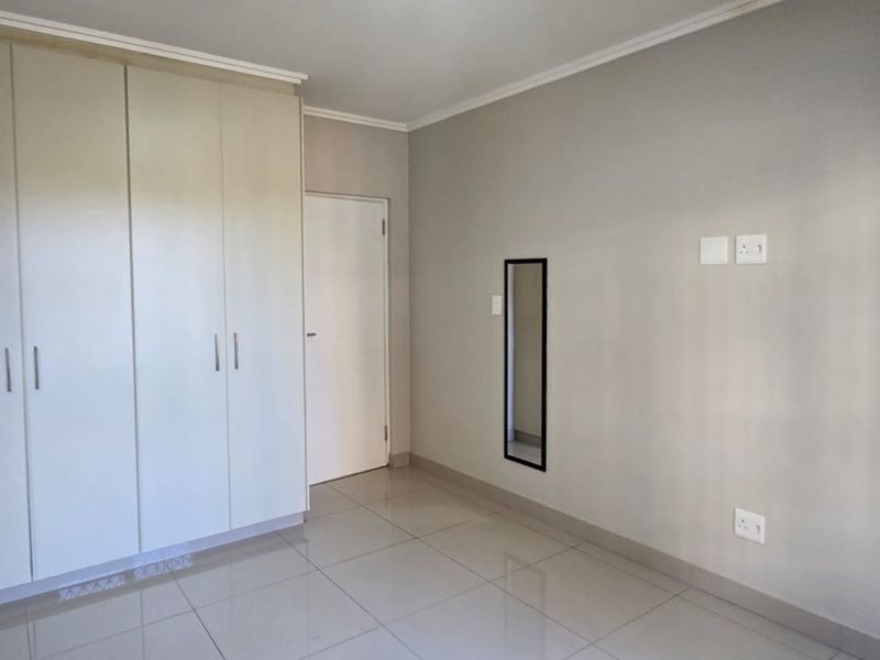 A clean, empty bedroom featuring neutral tiled flooring, built-in cupboards, and a simple, modern layout ready for personalization.