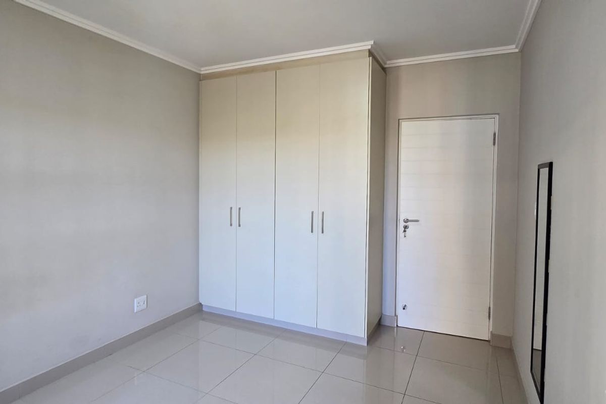 A clean, empty bedroom featuring neutral tiled flooring, built-in cupboards, and a simple interior door, offering a blank canvas for personalization.