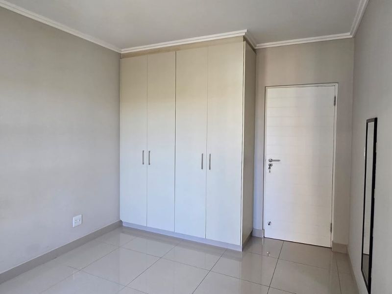 A clean, empty bedroom featuring neutral tiled flooring, built-in cupboards, and a simple interior door, offering a blank canvas for personalization.
