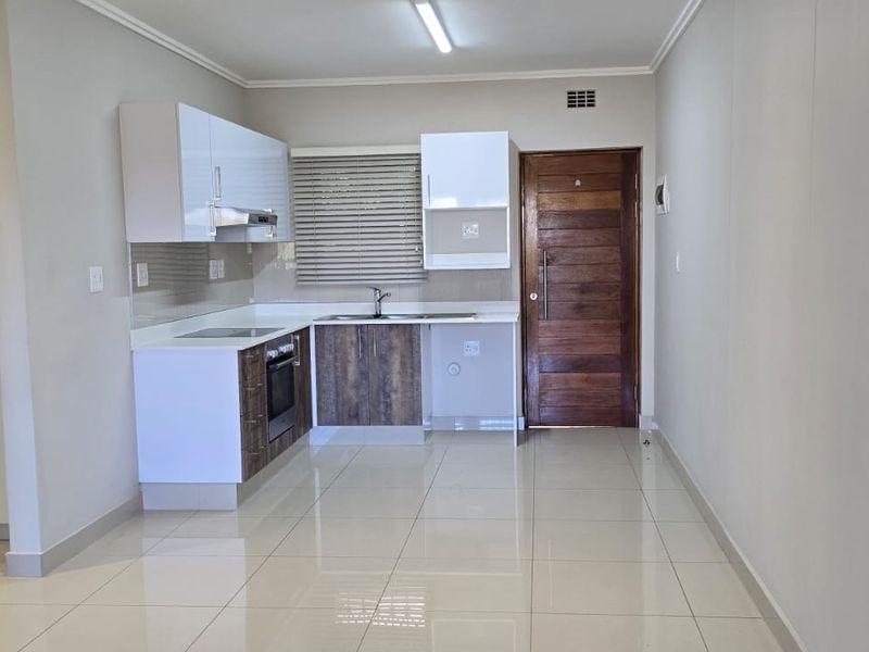 An open-plan kitchen area featuring modern cabinetry, built-in appliances, and tiled flooring, presented in a clean, vacant state.