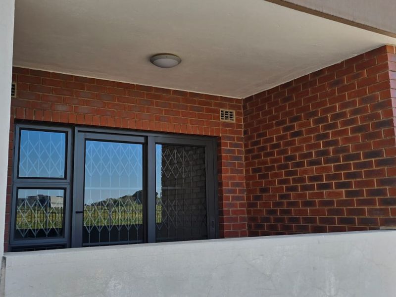 A covered patio area featuring exposed brick walls, a concrete balustrade, and a sliding glass door with security gate access.