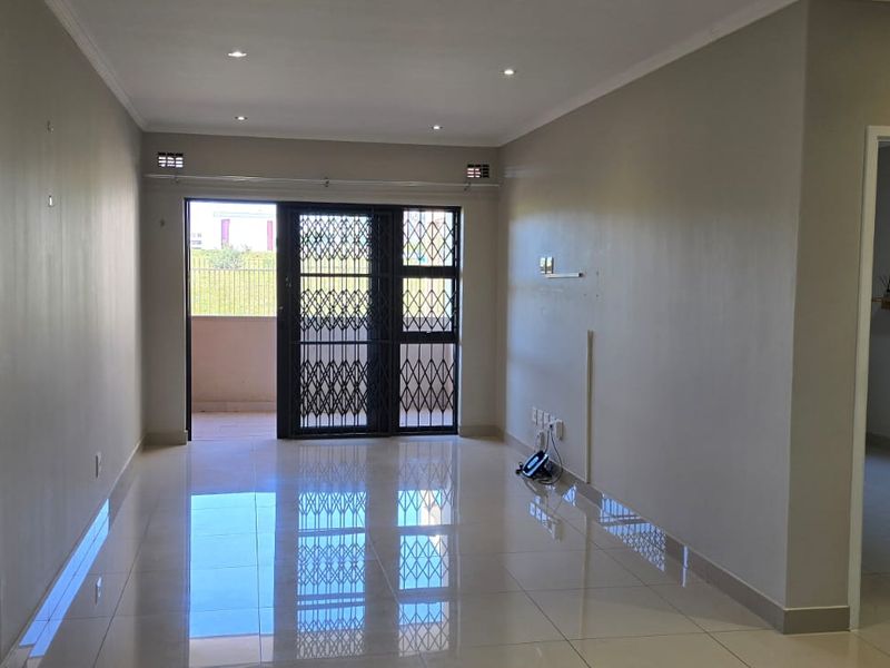 Spacious, empty living area featuring polished porcelain floor tiles, recessed downlighting, and a secure sliding door leading to an outdoor balcony.