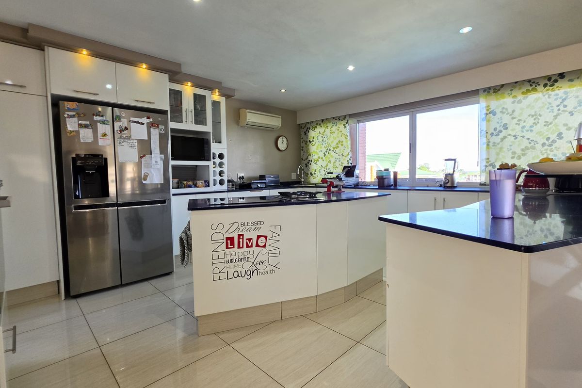 Modern kitchen featuring white cabinetry, dark stone countertops, a central island, and tiled flooring with integrated lighting and air conditioning.
