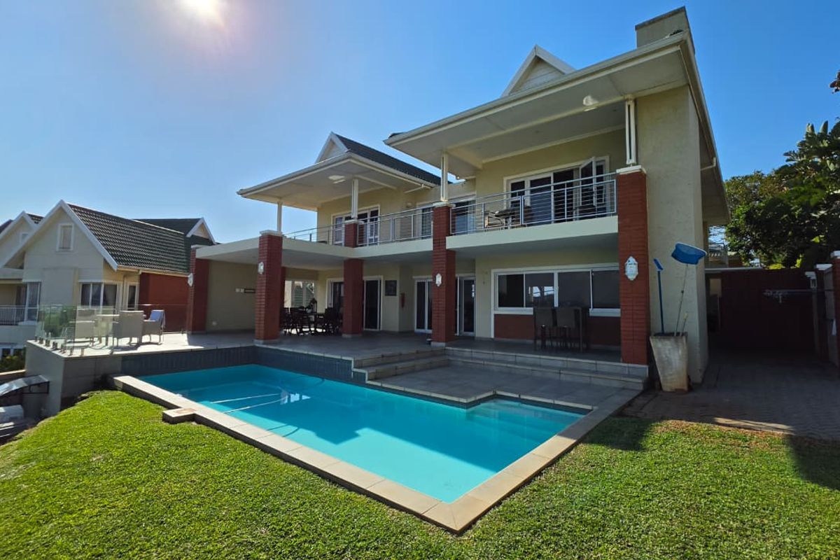 Rear view of the property featuring a swimming pool, paved deck, covered patio, and an upper-level balcony with metal railings.