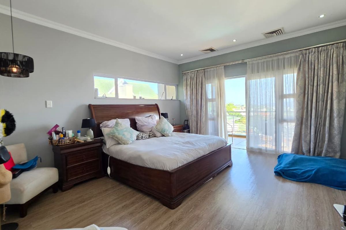 Spacious bedroom featuring laminate flooring, recessed lighting, ducted air conditioning, and sliding glass doors providing access to a private balcony.