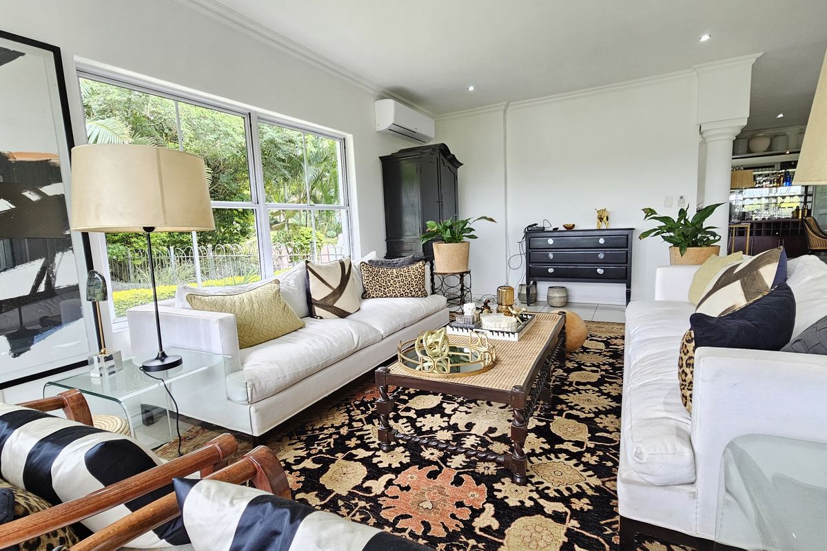 A bright and spacious living room featuring large windows with garden views, recessed lighting, and a wall-mounted air conditioning unit.