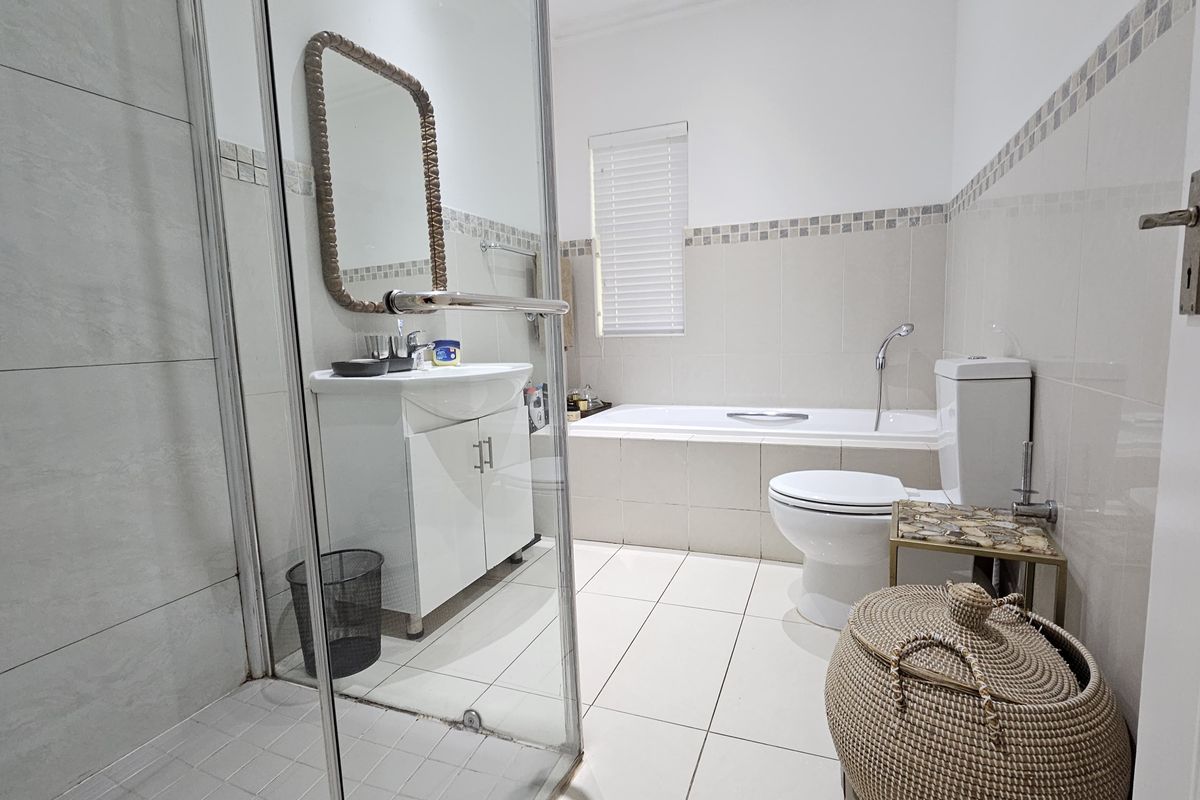 A well-maintained bathroom featuring a glass-enclosed shower, a built-in bathtub, a vanity unit, and neutral wall and floor tiling.