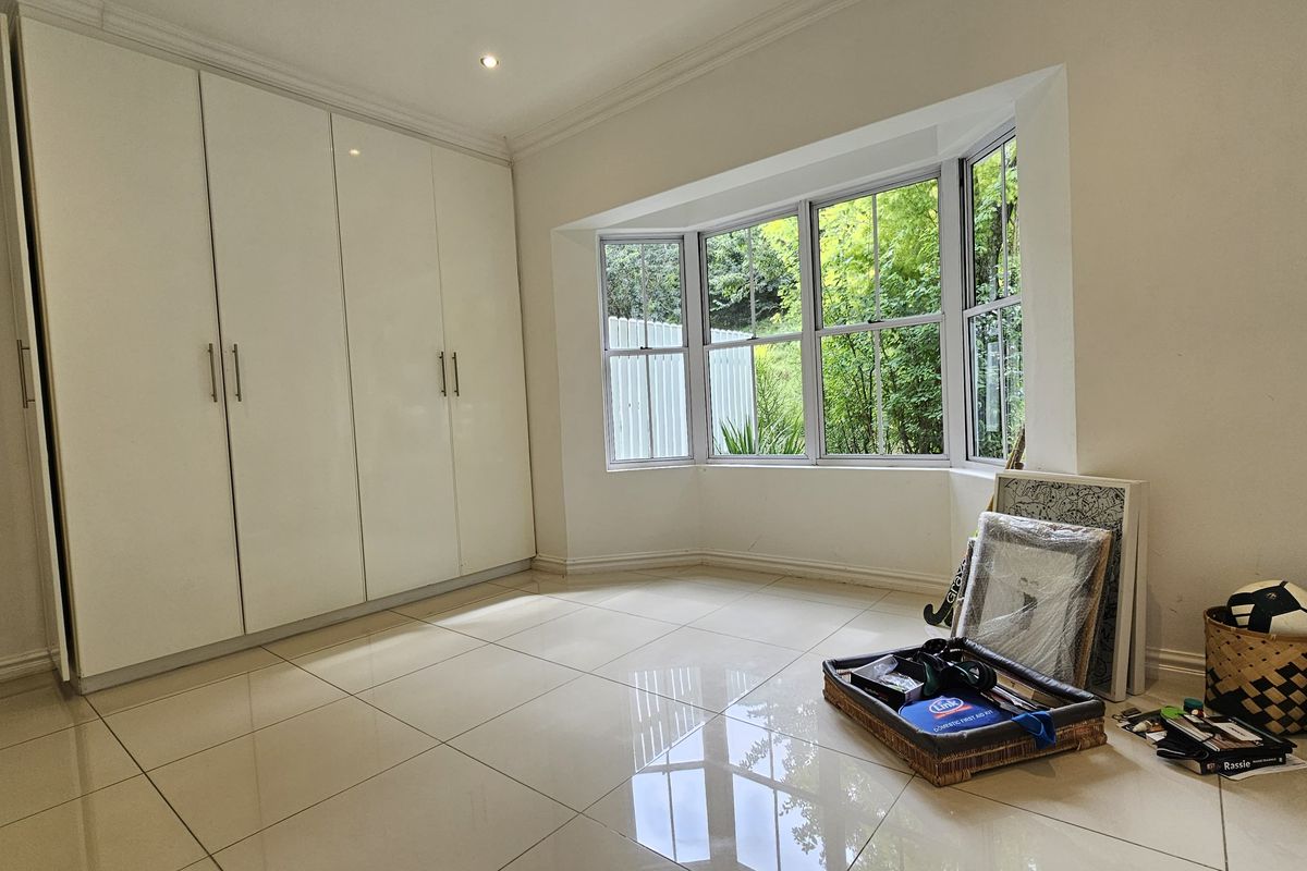 A bright bedroom featuring large built-in cupboards, polished tiled flooring, and a charming bay window overlooking the garden.